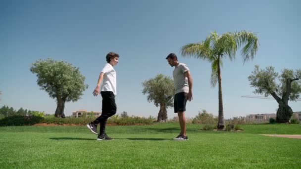 Kişisel antrenörü olan genç bir adam koordinasyon ve parktaki çimlerin üzerinde hareket dengesi için tek bacağının üzerine çömeliyor. Fonksiyonel eğitim. — Stok video