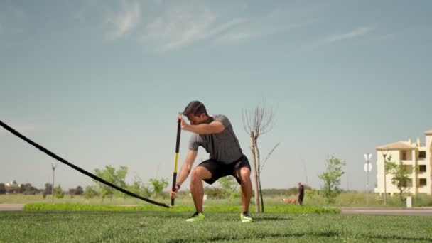 A man of European descent trains with aerobic equipment rubber bands and sticks from the outside. Summer for endurance. — Stock Video