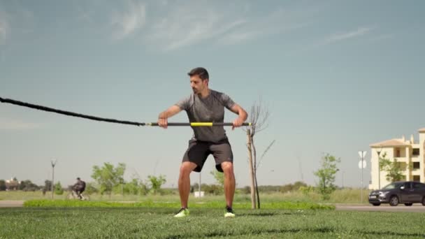 A man of European descent trains with aerobic equipment rubber bands and sticks from the outside. Summer for endurance. — Stock Video