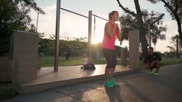 Formazione femminile europea nel parco con un personal fitness trainer. Esercizi sugli squat delle gambe e camminando di lato nel parco. — Video Stock