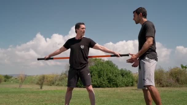 Treinador de fitness em treinamento funcional acompanha um homem em exercícios e reabilitação de costas de fora no verão. — Vídeo de Stock