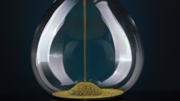 An hourglass made of yellow metal shavings passes through a funnel, symbolizing the concept of time in motion. — Αρχείο Βίντεο