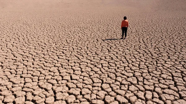 Silhouette d'un homme sur une terre sablonneuse fissurée vide pas fertile lors d'une sécheresse. Le concept de catastrophe écologique sur la planète. — Photo