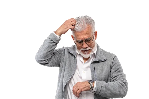 En äldre stilren man, gråhårig och med skägg, kliar sig i huvudet och tittar på klockan. Begreppet punktlighet och disciplin. — Stockfoto