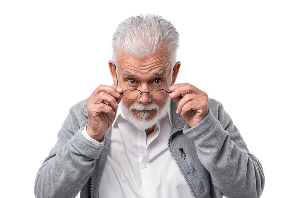 En äldre stilren man i glasögon med skägg och grått hår ser underifrån och håller i glasögon med händerna. — Stockfoto