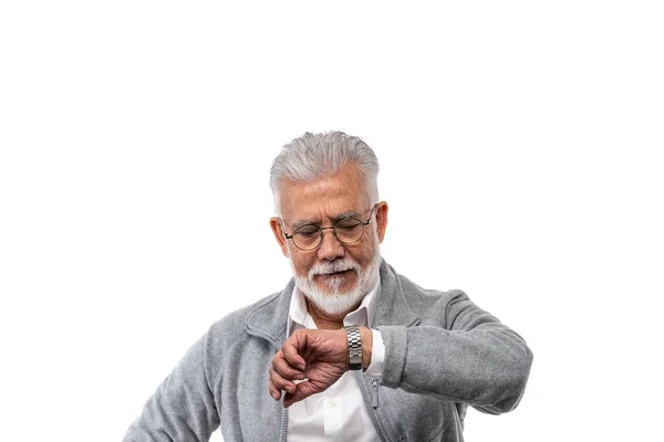 En äldre stilren man gråhårig och med skägg på en vit isolerad bakgrund tittar på sin klocka. Begreppet punktlighet och disciplin. — Stockfoto