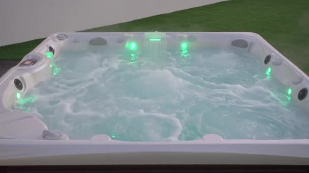 Close-up van het oppervlak van een moderne hot tub voor ontspanningstherapie en revalidatie in een hotel. Bubbels water in een bad onder zuurstofdruk 's Avonds buiten met lichten — Stockvideo