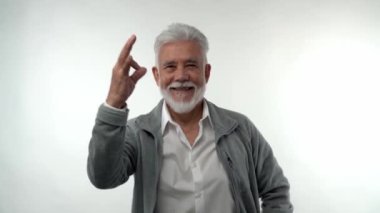 Gri sakallı ve saçlı şık yaşlı adam, beyaz izole bir arka planda her şeyin yolunda olduğunu gösteriyor. Emeklilik modası karakteri.