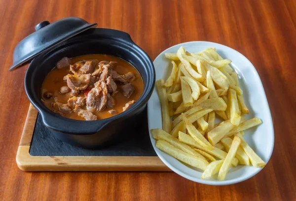 Las entrañas cocidas, los riñones, los ombligos y la carne en la salsa acompañada de las patatas fritas en la bandeja en el plato a la mesa de madera. —  Fotos de Stock