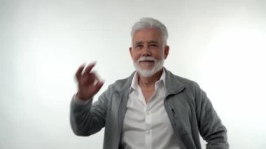 Gri sakallı ve saçlı şık yaşlı adam, beyaz izole bir arka planda her şeyin yolunda olduğunu gösteriyor. Emeklilik modası karakteri.