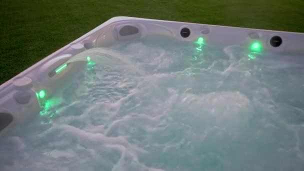 Close-up van het oppervlak van een moderne hot tub voor ontspanningstherapie en revalidatie in een hotel. Bubbels water in een bad onder zuurstofdruk 's Avonds buiten met lichten — Stockvideo
