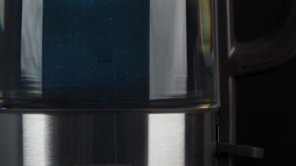 Osoba stiskne tlačítko skleněné konvice, aby se vařila voda. Bubliny stoupají v modrém světle. pomalý pohyb. — Stock video