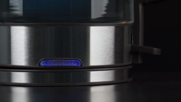 A persons fingers press the button of a glass kettle to boil water. Bubbles are rising in the blue light. low motion. — Video Stock