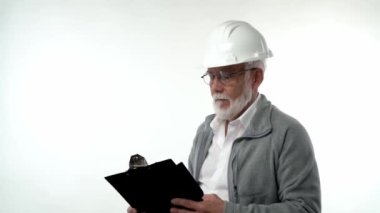 İnşaat kaskı takmış sakallı yaşlı bir adam beyaz arka plandaki yazı tahtasına kalemle notlar yazıyor. Yüksek kaliteli FullHD görüntüler