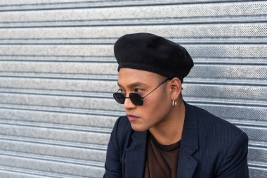 Makyajlı, şık bir şapka takan, güneş gözlüğü takan, metal bir kürtanın üstünde izole edilmiş genç, Latin bir gay. LGBT.