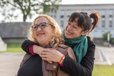 Gülümseyen lezbiyen bir çiftin portresi. Dışarıda yan yana dururken birbirlerine sarılıyorlar.