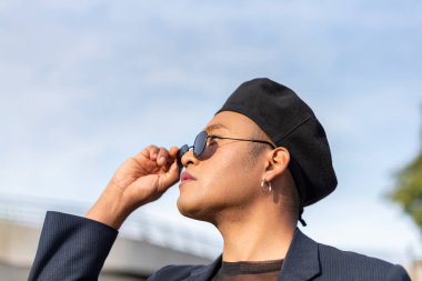 Makyajlı, şık bir şapka takan ve güneş gözlüğünün üstünden bakan genç, latin eşcinsel adam. LGBT. Boşluğu kopyala 