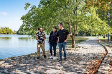 Bir grup arkadaş parkta yürüyor ve birbirleriyle canlı canlı sohbet ediyorlar. Arkaplan resmedilmiş görünümü