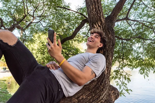 Young Man Leaning Tree Trunk Laughing Using His Smartphone — Φωτογραφία Αρχείου