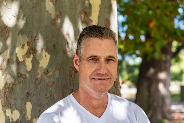 A handsome man leaning on a tree and looking at the camera