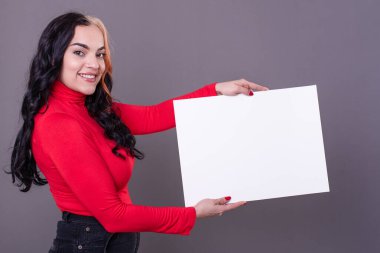 Beautiful woman holding a blank sign against a grey background
