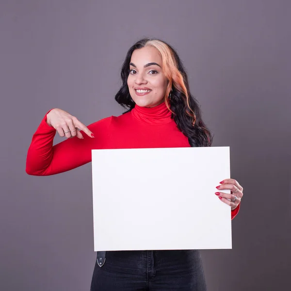 Beautiful woman pointing at a blank whiteboard against a grey background