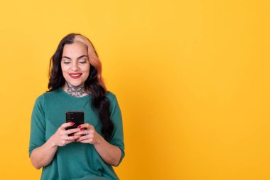 Portrait of an attractive woman using smart phone over yellow background. Studio shot.