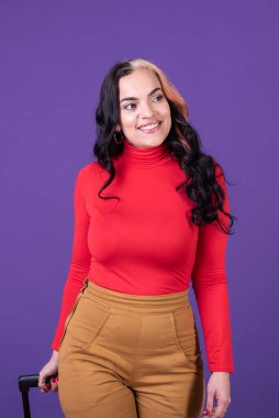 Happy woman traveler holding her suitcase while walking against purple background. Studio shot