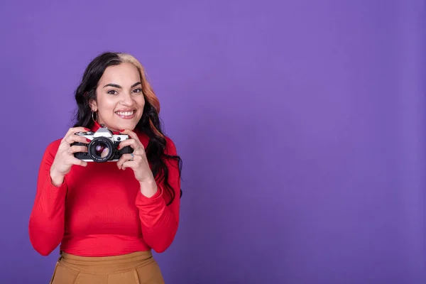 Attractive young lady taking a photo with her film camera over a violet background.  Copy space. Studio shot.
