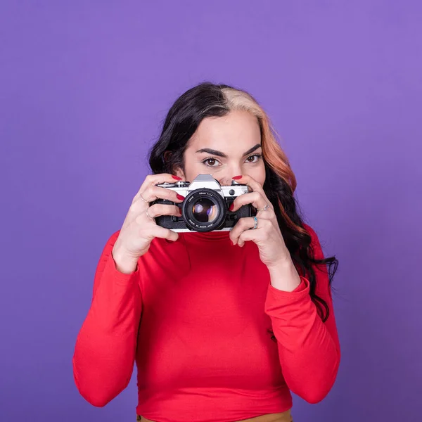 Attractive young lady taking a photo with her film camera over a violet background.  Studio shot.