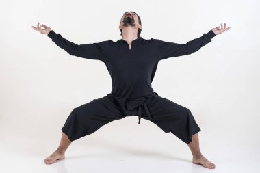 Siyah giyinmiş bir adam beyaz arka planda yoga yapıyor..