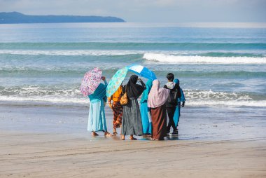 Müslüman kadınlar ve Endonezya 'nın Bali sahilinde denize bakan genç bir adam.