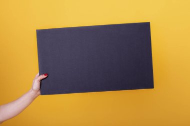 Fotokopi alanı için boş bir siyah sayfa posteri ve sarı arka planda bir maket tutan bir kadın..