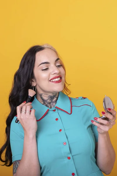 Attractive Woman Applying Face Powder over yellow Studio Background