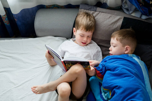 little brother reads a book on the bed for an elder. Friendship between brothers. Love for reading. Lark and owl among people. 2 boys on the bed are reading one book. Bedtime stories