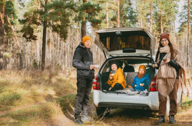 İki çocuklu bir aile ormanda bir arabanın bagajında piknik yapıyor. Ormanda aile ve samimi yürüyüşler. Kışın ve sonbaharda arabayla seyahat etmek. Koronavirüs sırasında yürümek