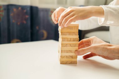Erkek çocuğun elleri, evde Jenga 'da masanın üzerinde beyaz bir tişörtle oynuyor. Çocuklar ve yetişkinler için masa oyunları. Aletsiz bir eğlence. Tatillerde evde oyunlar. çocuk tahta bloklarla oynar.