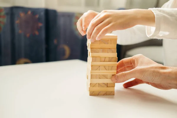 Erkek çocuğun elleri, evde Jenga 'da masanın üzerinde beyaz bir tişörtle oynuyor. Çocuklar ve yetişkinler için masa oyunları. Aletsiz bir eğlence. Tatillerde evde oyunlar. çocuk tahta bloklarla oynar.