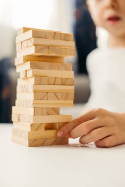 Erkek çocuğun elleri, evde Jenga 'da masanın üzerinde beyaz bir tişörtle oynuyor. Çocuklar ve yetişkinler için masa oyunları. Aletsiz bir eğlence. Tatillerde evde oyunlar. çocuk tahta bloklarla oynar.