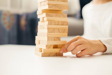 Erkek çocuğun elleri, evde Jenga 'da masanın üzerinde beyaz bir tişörtle oynuyor. Çocuklar ve yetişkinler için masa oyunları. Aletsiz bir eğlence. Tatillerde evde oyunlar. çocuk tahta bloklarla oynar.