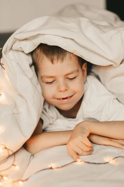 Retrato Menino Sorridente Deitado Sob Cobertor Branco Com Uma Grinalda — Fotografia de Stock