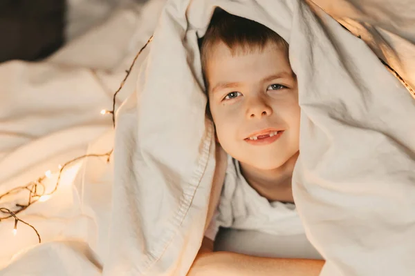 Портрет Усміхненого Хлопчика Лежить Під Білою Ковдрою Гірляндою Дитячий Різдвяний — стокове фото