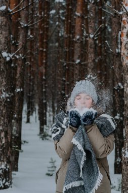 girl blows snow off her hands. A girl in a hat throws snow in the winter forest. Happy winter holidays. Love for winter. Winter in the north.