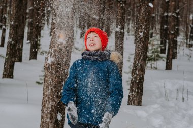 A boy walks in the snow in the winter forest. A child throws snow over his head. Happy winter holidays with snow