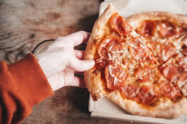 Ellerinde büyük bir dilim pepperoni pizza, yakın plan. Lezzetli İtalyan atıştırması. Salamlı pizza..