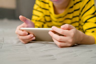 Çocuk elinde bir telefonla kanepede uzanıyor, yakın plan. Çocuk evde, telefonda oynuyor. Telefonla eğlence..