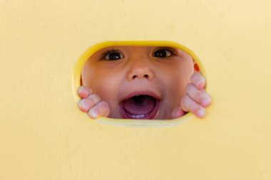 Çocuk parkında oynayan tatlı bir erkek bebek. Çocuk sarı delikten kameraya bakıyor