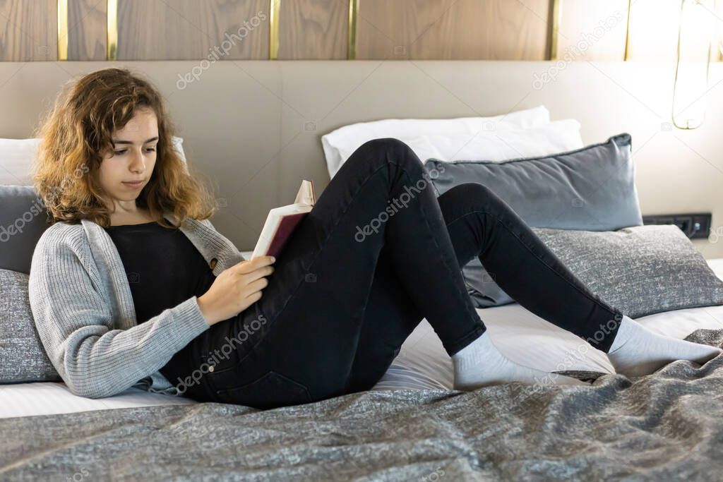 Teenager girl reading book on her bed