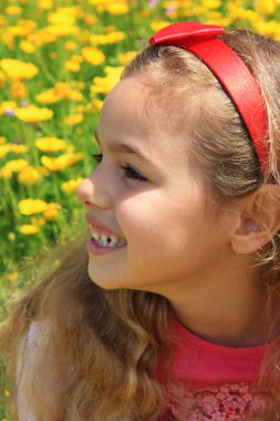 Curly little girl with a red bow in her hair. Girl on green meadow among yellow flowers. Allergy to flowers and pollen