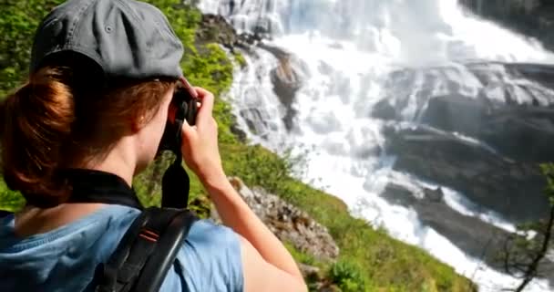 Kinsarvik, Hordaland, Norge. Ung kvinna Lady turist resenär tar bilder av vattenfall Nyastolfossen i Hardangervidda Mountain Plateau. Nyastolsfossen är känd populär destination — Stockvideo